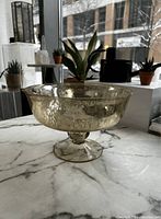Clear hammered gold-colored glass footed vase on marble countertop in front of window.