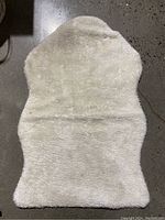 White faux fur shaped rug showing texture and condition on concrete floor