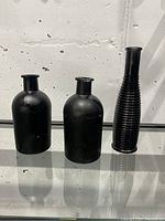 Three black spray painted glass vases including two bottle-shaped and one tall ribbed cylindrical vase.