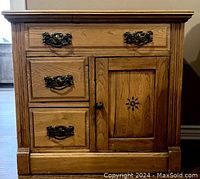 Front view showing three drawers and door with carved sunburst detail and decorative handles