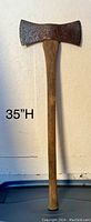 Photo showing the entire double bit axe measuring 35 inches in height, with a wooden handle and a rusty metal double bit axe head.