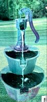 Photo of the assembled water fountain with water flowing from hand pump into two tiered buckets outdoors.