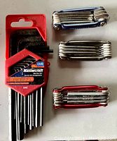 Photo showing four hex key sets: one Mastercraft 13-piece SAE set in red plastic holder, and three foldable multi-size chrome metal sets in silver and red holders arranged on flat surface.