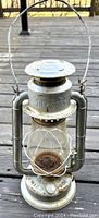 Front view of vintage silver Beacon's lantern on wooden surface showing rust on base and fuel cap area.