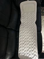 Front view of white full body bath soak mat with built-in pillow on black leather surface.