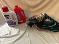 Bissell Power Carpet Cleaner handheld unit with two bottles of carpet cleaning solutions placed on fabric background.