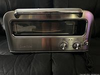 Front exterior view of stainless steel pizza oven showing Breville logo, glass window, control knobs and power cord