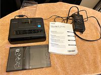 Canon SELPHY CP1200 photo printer with power adapter, photo paper case, and manual on a brown surface.