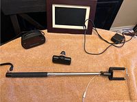 Photo showing all items on a towel - selfie stick, digital photo frame, small cylindrical device, power charger, alarm clock