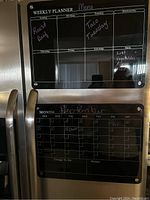 Photo showing both magnetic dry erase boards mounted on stainless steel surface: a weekly planner board and a monthly calendar board, both with handwritten notes.