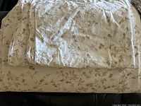 Image showing a white duvet cover with beige floral vine design folded on a black leather surface.