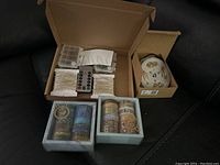 Box with two spools of silver wire fairy string lights, two plastic battery cases, a remote control, and a pack of metallic gold wire string lights.