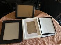 Collection of multiple black and white 8x10 frames on a brown textured cloth surface, some stacked and some displayed upright.