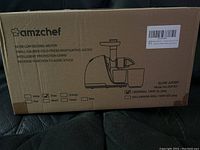 Box of Amzchef juicer showing product information and specifications including 60 dB low decibel motor, 150 watt power, reverse function, and intelligent protection chips.