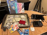 Photo of various items including a charging station, photo tray, hole punch, colorful stationery, external hard drive, batteries, and charging cables.