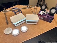 Wide view of all items showing two white toilet paper holders with shelves, three round LED puck lights, two LED panel lights with remotes, a stainless steel horizontal bar, and a wall hook.
