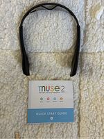 Muse 2 black brain sensing meditation headband with a cloth background, showing the entire headband and Quick Start Guide underneath.