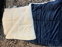 Comforter laid flat showing the white sherpa fleece side and edges of the blue velvet side underneath
