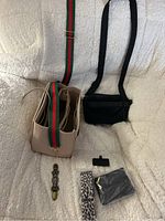 Full view of all items together: beige purse bag insert, black crossbody bag, multiple straps and accessories on white textured background.