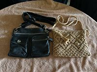 Photo showing both the black leather Roots crossbody purse and the beige crocheted shoulder bag side by side on a beige fabric background.
