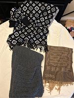Photo showing the three scarfs laid out on a white surface including black and white patterned scarf, gray knitted scarf, and brown patterned scarf.