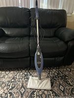 Full view of Shark floor steamer upright on floor with microfiber pad attached, showing blue and gray plastic body.
