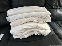 Stack of five white/off-white fitted sheets folded and stacked on black sofa