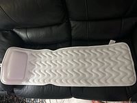 White bath soak mat with a cushioned headrest and zigzag textured surface laid out on a black couch.
