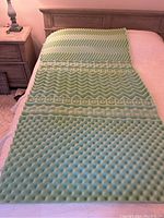 Foam mattress topper laid flat on a bed showing multiple textured comfort zones in light green foam.