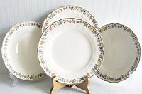 Four Grindley vintage salad plates displayed on plate stands showing floral pattern with pastel colors and gold trim.