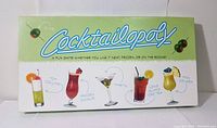 Full view of the green and white Cocktailopoly game box with cocktail illustrations and title visible