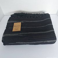 Folded black and grey striped cotton handwoven rug with hanging tag indicating brand Rivancia and material 100% cotton.