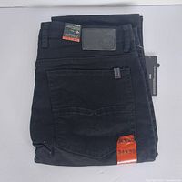 Folded black denim jeans with size 34x30 sticker and rear pocket visible.