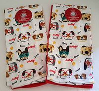Front side of two kitchen towels showing dog face and 'woof' print pattern with red trim.