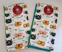 Two folded kitchen towels showing cat faces with glasses print and Pets at Home tag