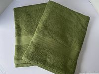 Two olive green bath towels folded, showing texture and woven band detail.
