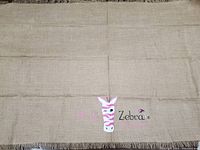 Full view of the large burlap mat showing the coarse woven texture and fringe edges with a small embroidered or printed Pink Zebra logo.