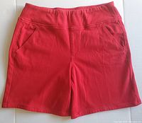 Front view of red Bermuda shorts showing waistband, front pockets, and overall texture of the fabric.