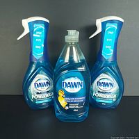 Front view of two Dawn Platinum Powerwash spray bottles on either side of one Dawn Ultra squeeze bottle, all blue liquid, all 473 ml.