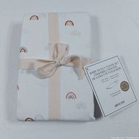 Folded baby duvet cover set tied with beige ribbon on white background. White fabric with small rainbow print.