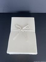 Folded taupe fitted sheet tied with matching fabric ribbon on a black surface.