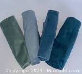 Four velvet decorative cushion covers in various shades of green and blue, rolled and placed side-by-side.