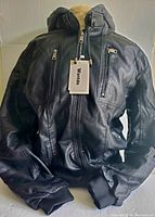 Full view of the new black faux leather jacket showing hood, sleeves, and front zippered pockets with tags attached.