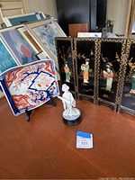 Decorative plate, black lacquer screen, and porcelain figurine on a table.