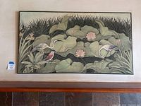 Front view of large rectangular Asian fabric wall art placed above a wooden ledge, showing the entire artwork of birds and lotus flowers.