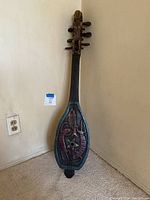 Full view of the Asian stringed instrument standing against the wall, showing its carved and painted body with fish and lobster motifs.