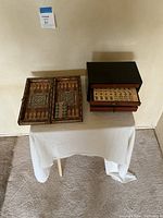Both backgammon board and mahjong box displayed on table, backgammon board open showing inlay and pieces, mahjong tiles visible