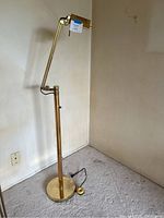 Full view of brass floor lamp showing base, vertical stand, adjustable arm, and head with Maxsold tag.