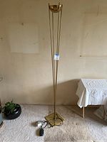 Full view of brass floor lamp showing four metal rods, square base, bowl shade, cords on floor