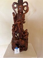 Full view of the carved wooden Asian sculpture with a large central figure and two smaller figures at the base.